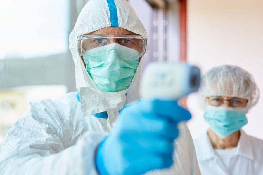 A nurse, dressed in full PPE, takes someones temperature.